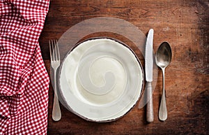 Traditional cutlery and plate, red checkered tablecloth on wooden table, top view