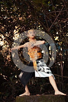 A Traditional dancer with golden clothes and a golden crown posing bravely in the jungle