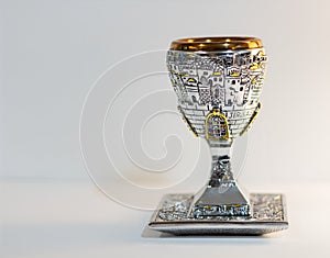 Traditional, decorative Jewish kiddush cup. Silver cup with saucer filled on a blurred background