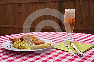 Traditional deep fried chicken schnitzel served with mashed potatoes and pickled cucumbers with lager beer in the glass.