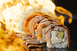 Traditional delicious fresh sushi roll set on a black background with reflection and fire, close up. Sushi roll with