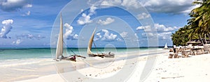 Traditional dhows on a beach on the coast of Zanzibar. Boats in turquoise ocean and blue sky, panorama.