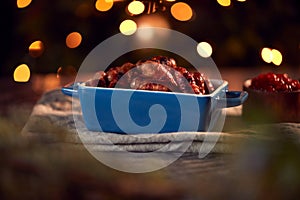 Traditional Dish Of Christmas Pigs In Blankets On Table Set For Meal With Tree Lights In Background