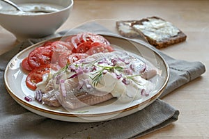 Traditional Dutch salted herring fillets also called maatje with cream sauce, red onions, dill garnish and tomato salad served on