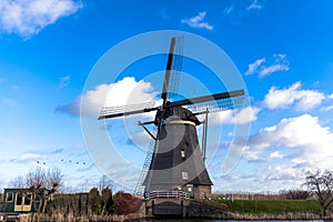 Traditional dutch windmill near the canal. Netherlands. Old windmill stands on the banks of the canal, and water pumps. White clou