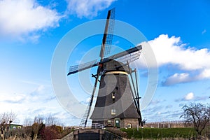 Traditional dutch windmill near the canal. Netherlands. Old windmill stands on the banks of the canal, and water pumps. White clou
