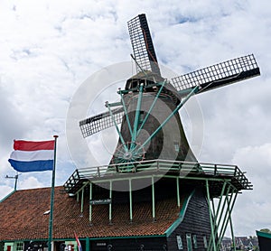 Traditional Dutch windmill under an overcast sky with the flag of the Netherlands flying in a strong wind