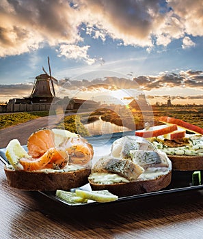Traditional Dutch windmills with fishplate salomon and cod sandwiches against sunset in Zaanse Schans, Amsterdam area,
