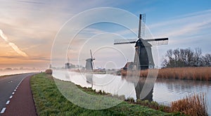 Traditional Dutch windmills near the canal during a misty morning.