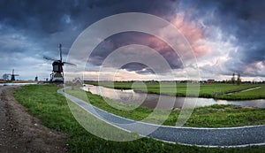 Traditional dutch windmills near water canals with cloudy sky, landscape