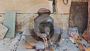 Traditional earthen pot on a makeshift outdoor stove with firewood used for cooking boiling water in rural settings