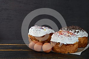 Traditional Easter bread or cake with white glaze and multicolored rainbow sprinkle decorated with eggs on the black wooden table