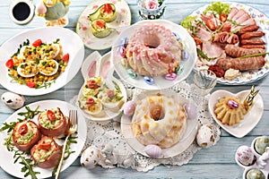 Traditional Easter breakfast with salads, deviled eggs, cold cuts and pastries on blue wooden table