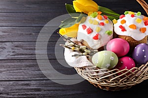 Traditional Easter cakes and eggs in wicker basket on dark table. Space for text
