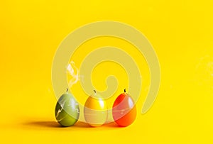 Traditional Easter decor. Group of bright paraffin extinguished candle with smoke in the shape of colorful eggs on warm yellow