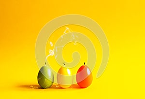 Traditional Easter decor. Group of bright paraffin extinguished candle with smoke in the shape of colorful eggs on warm yellow