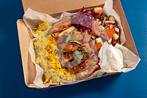 Traditional Eastern Mediterranean takeaway meal of grilled chicken, yellow rice, fresh salad and yoghurt in cardboard