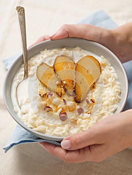 Traditional english breakfast. Woman holds bowl of cereal oatmeal or porridge with nuts and pears. Close up shot. Soft focus