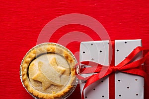 Traditional English Christmas dessert pastry mince pies in muffin tins sprinkled with sugar gift bow tied with ribbon on red