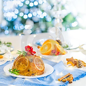 Traditional English Christmas pudding decorated with oranges and flowers in a festive table setting with fruits, spices