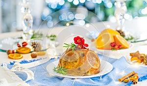 Traditional English Christmas pudding decorated with oranges and flowers in a festive table setting with fruits, spices