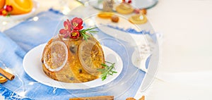 Traditional English Christmas pudding decorated with oranges and flowers in festive table setting with fruits and spices, blue