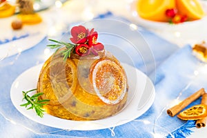 Traditional English Christmas pudding decorated with oranges and fresh flowers in a festive table setting with fruits