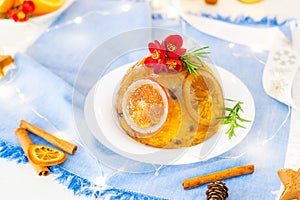 Traditional English Christmas pudding decorated with oranges and fresh flowers in a festive table setting with fruits, spices and