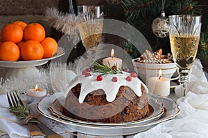 Traditional english Christmas steamed pudding with winter berries, dried fruits, nut in festive setting with Xmas tree, burning ca