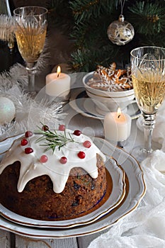 Traditional english Christmas steamed pudding with winter berries, dried fruits, nut in festive setting with Xmas tree, burning ca