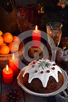 Traditional english Christmas steamed pudding with winter berries, dried fruits, nut in festive setting with Xmas tree, burning ca