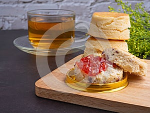 Traditional English style scones delicious freshly baked homemade with strawberry jam on a plate on wooden cutting board