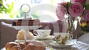 Traditional English tea time, Afternoon tea ceremony with cuppa tea, croissants, crackers and biscuits on hight tea stand in pink 