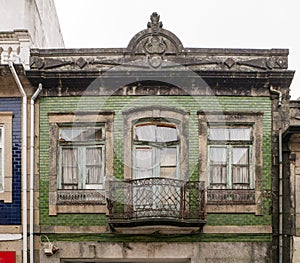 Traditional facade of old Portuguese architecture house with green tiles and metal balcony. Weathered, broken windows.
