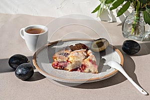 Traditional The Famous plum torte, pie. Piece on plate with cup of tea, teaspoon and plums on table in sunlight