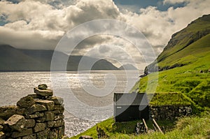 Traditional faroese shed ath the edge of the cliff, Mikladalur, Kalsoy, beautiful view on the sea and islands Kunoy and Bordoy, photo