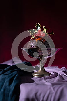 Traditional festive Christmas fruit pudding dessert, decorated with cherries and leaves, set in a classic warm red and purple