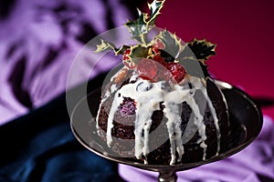 Traditional festive Christmas fruit pudding dessert, decorated with cherries and leaves, set in a classic warm red and purple