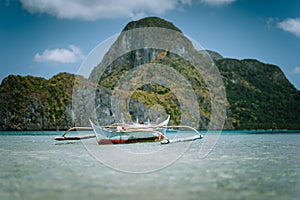 Traditional filippino banca boat in blue tropical lagoon at El Nido bay. Impressive karst mountains of Cadlao Island in