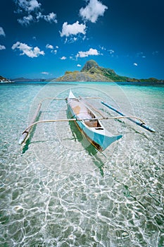 Traditional filippino fisher banca boat in blue lagoon at El Nido bay with Cadlao Island on Background. Palawan Island