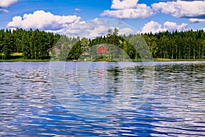 A traditional Finnish wooden cottage with a sauna and a barn on the lake shore. Summer rural Finland.