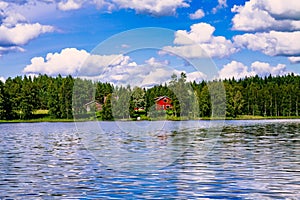 A traditional Finnish wooden cottage with a sauna and a barn on the lake shore. Summer rural Finland.