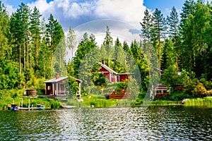 A traditional Finnish wooden cottage with a sauna and a barn on the lake shore. Summer rural Finland.