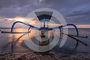 Traditional fishing boat on the beach during sunrise.  water reflection.  sanur beach bali