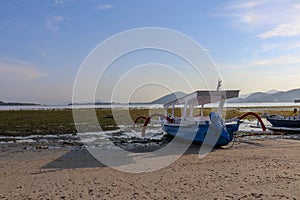 Traditional fishing boat moored at sandy beach using an anchor rope. Laminate boat with wooden roof tied up by shore at low tide.