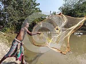 Traditional fishing by a fisherman throwing a spinning net in a pond