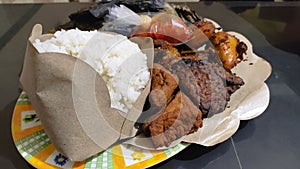 Traditional food from Indonesia, rice white grilled meat fried plantains traditional dish wrapped in banana leaves