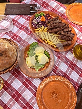 Traditional Food from Montenegro cevapi, butter, and bread on a red plaid tablecloth and ceramic plates