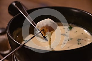 Traditional French cheese fondue in crockery black pot. Melted cheese on piece of grilled bread. French local cuisine. Hot food