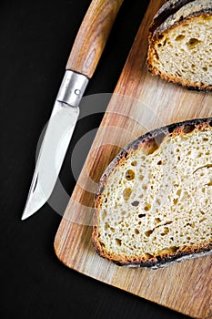 Traditional French country bread slices and pocket knife on a cutting board